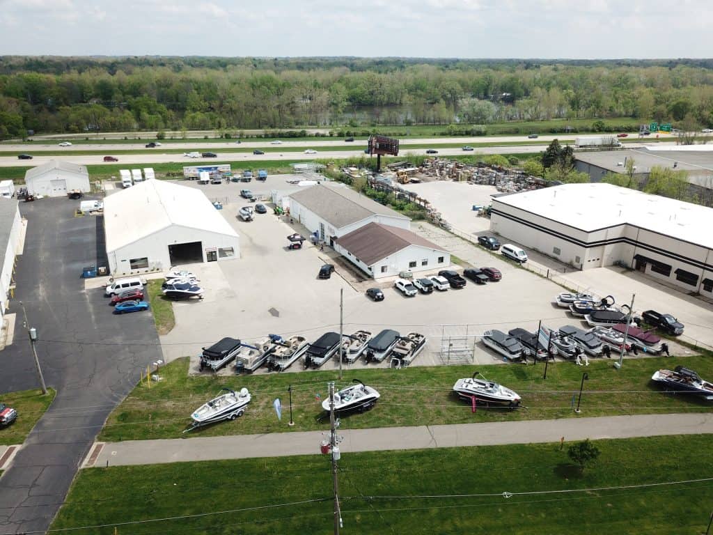 Aerial view of Hall's Sport Center showcasing boats, trailers, and vehicles for sale outside with surrounding commercial buildings and highway in background.