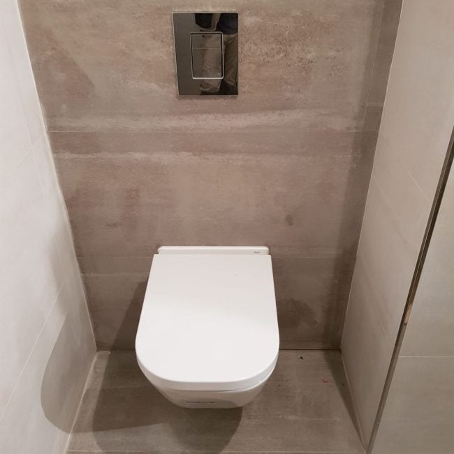 Sanitario de inodoro moderno con revestimiento en paredes y suelo de cerámica. Reformas integrales y obras en baños por Hammerman Reformas.