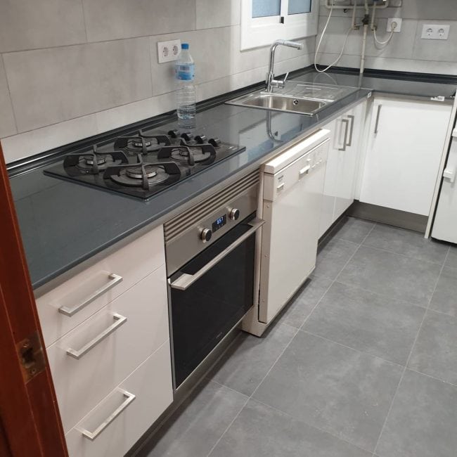 Renovación de cocina moderna con encimera de granito, horno, vitrocerámica y fregadero en reformas de calidad.