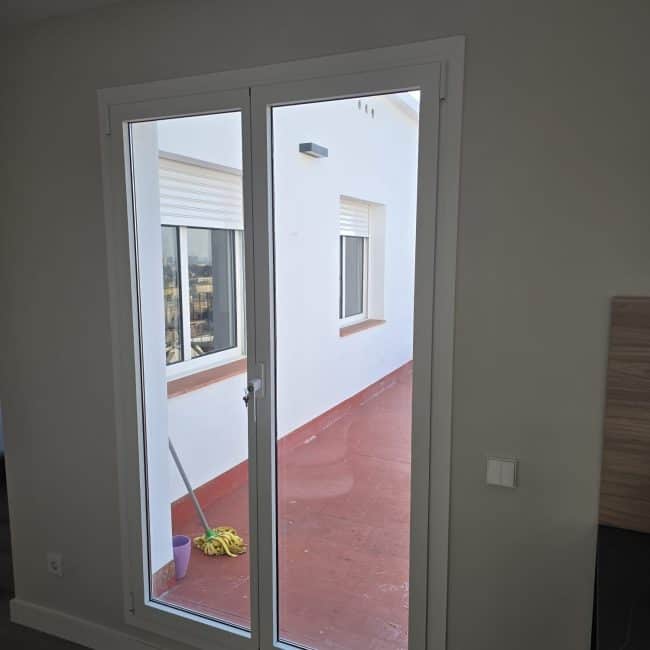 Puerta balcón de aluminio blanco con vista a terraza exterior en obra nueva.