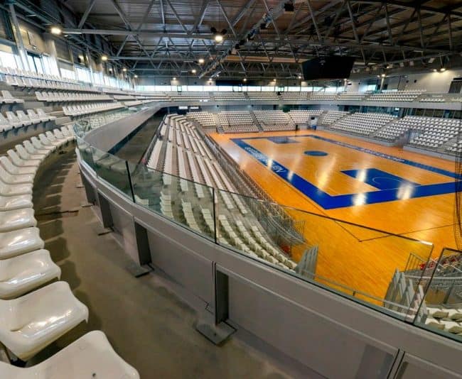 Pista de baloncesto en estadio cubierto con asientos modernos, ideal para reformas deportivas y acondicionamiento de instalaciones deportivas.
