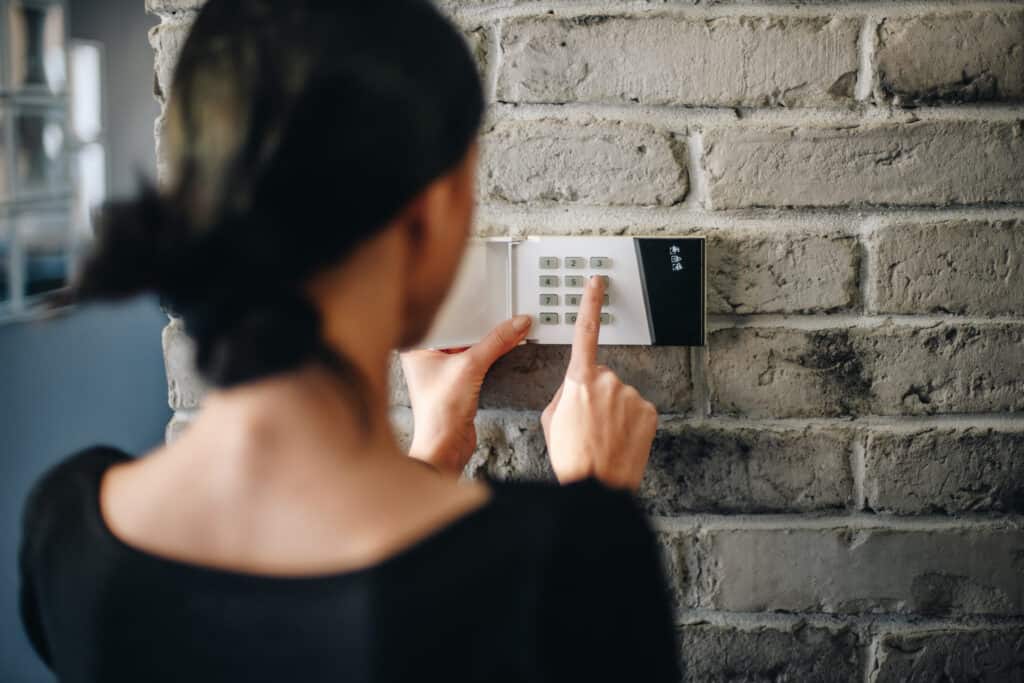 A young woman entering a PIN on an alarm system in her home