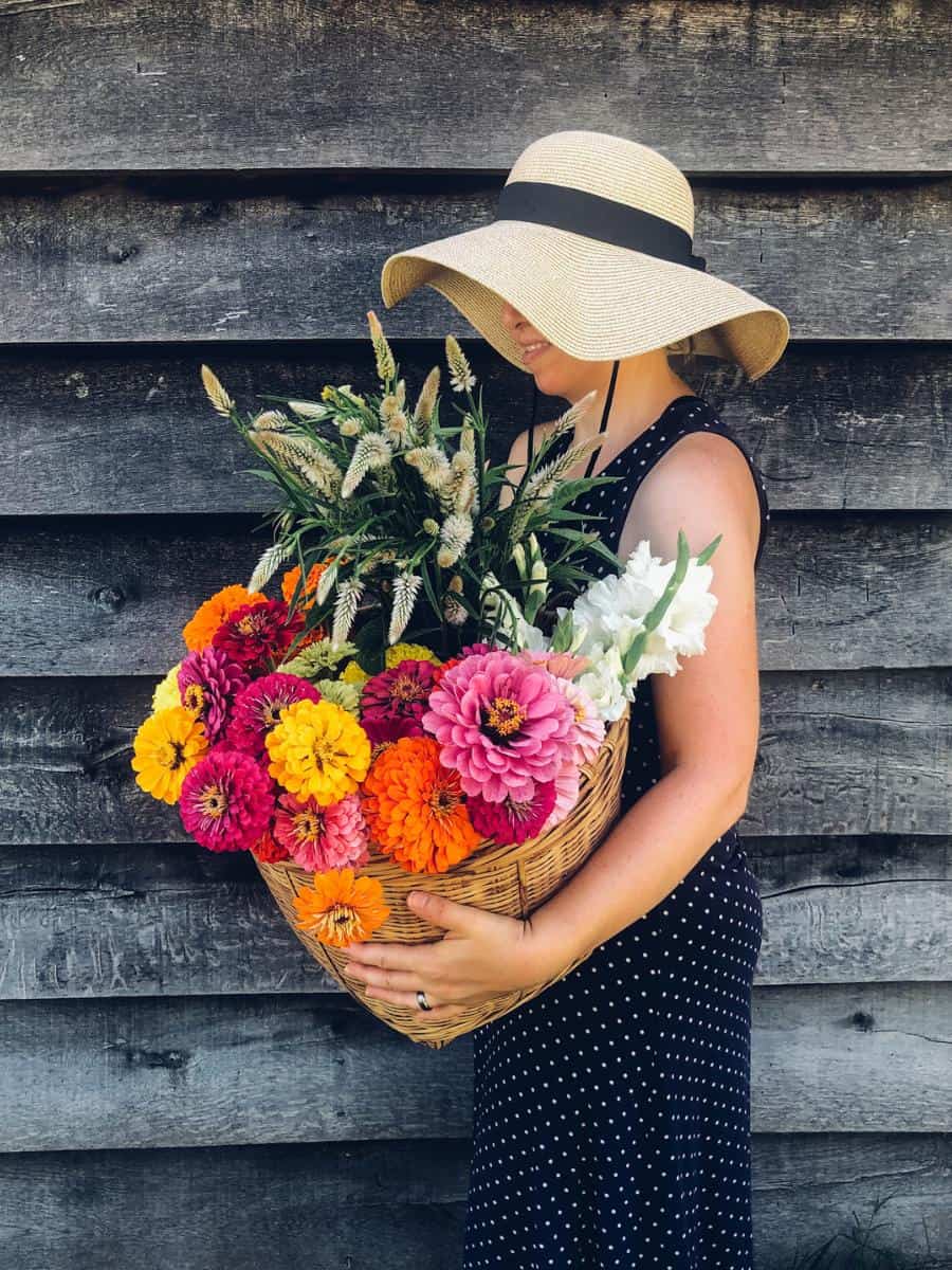 woman wearing a hat holding a basket of colorful flowers