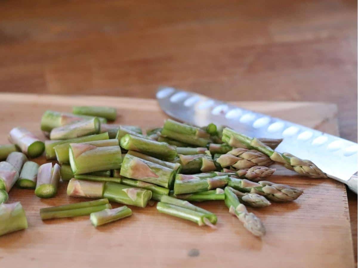 asparagus spears chopped on a wooden cutting board with a knife