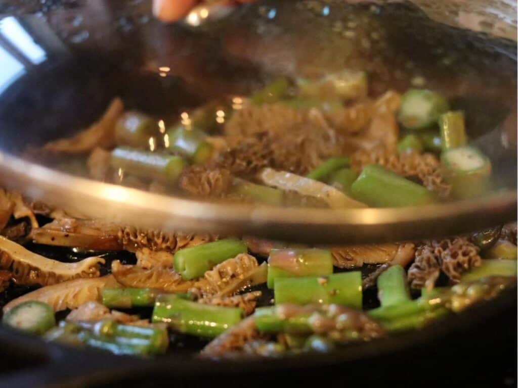 sautéed morels and asparagus in a cast iron pan with a glass lid