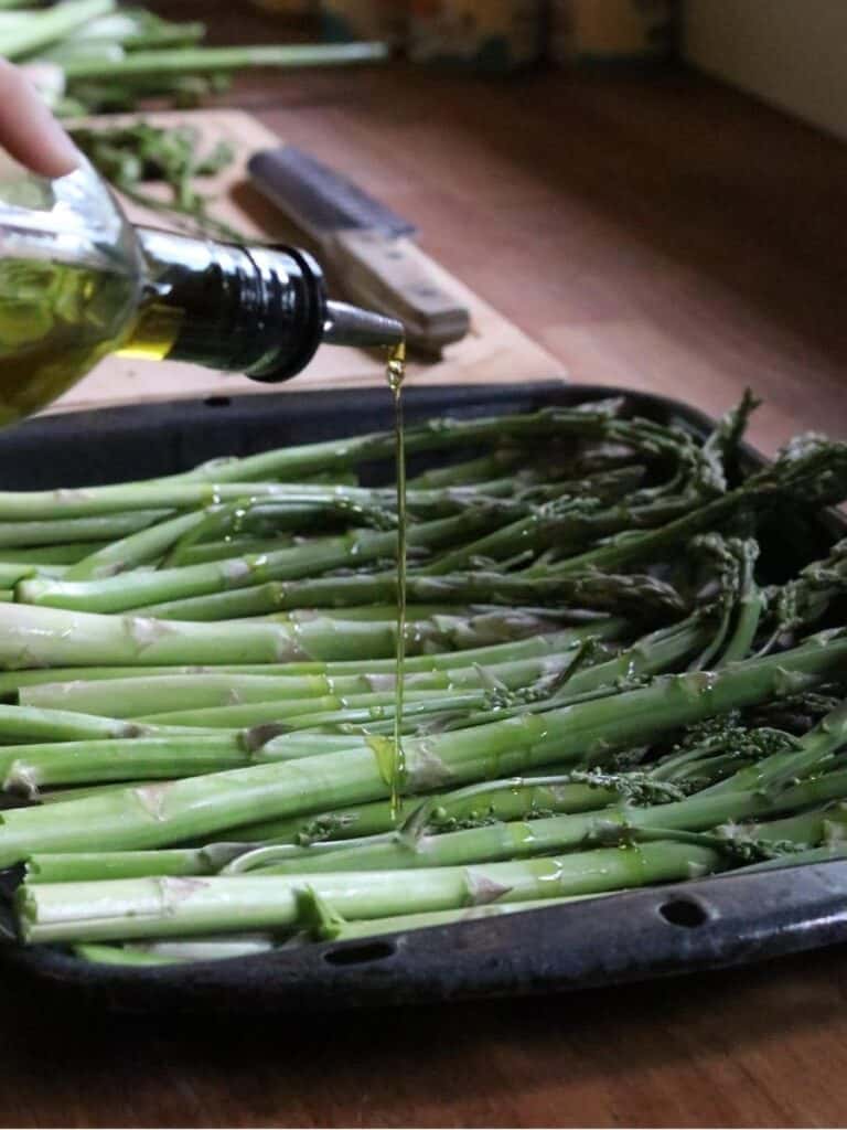 drizzling olive oil over a pan of asparagus for a roasted asparagus recipe