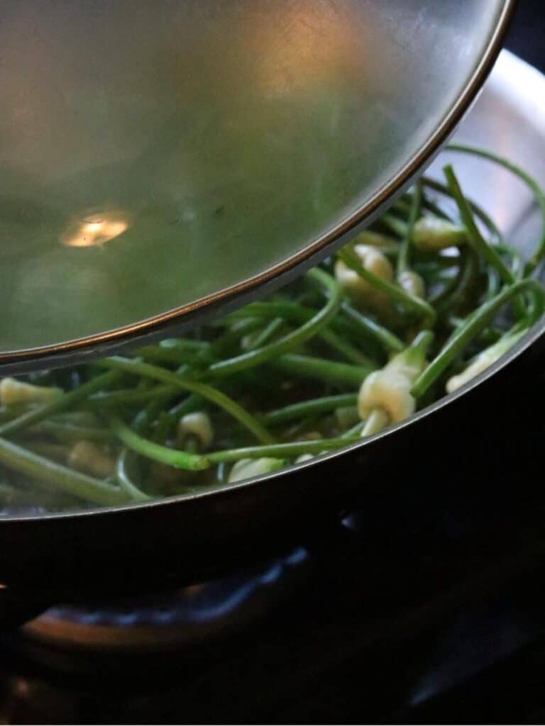 putting lid on pan to sauté garlic scapes