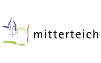 Mitterteich Das Logo zeigt links stilisierte Gebäudeumrisse in Blau, Gelb und Orange, rechts das Wort „Mitterteich“ in schwarzen Kleinbuchstaben. Das Gesamtdesign ist schlicht und farbenfroh.