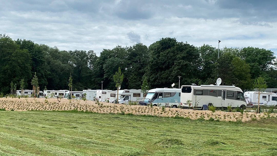 Rödental_Wohnmobilstellplatz_1080 Eine Wiese mit mehreren geparkten Wohnmobilen und Wohnwagen unter einem bewölkten Himmel. Im Hintergrund sind hohe Bäume zu sehen, die den Campingplatz umgeben.