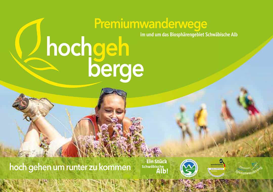 titel_hochgehberge_broschuere_1080 Eine Frau liegt im Gras und riecht lila Blüten. Im Hintergrund sind Wanderer unscharf zu sehen. Der Text lautet „Premiumwanderwege hochgehberge“ und „hoch gehen um runter zu kommen“ mit Logos am unteren Rand. Grün und Gelb dominieren das Bild.
