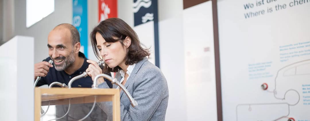 ausstellung2_1080 Ein Mann und eine Frau betrachten ein Exponat mit Röhren in einem Wissenschafts- oder Bildungszentrum. Der Mann lächelt, während er auf das Exponat blickt, während die Frau konzentriert wirkt. Im Hintergrund sind Informationstafeln zu sehen.