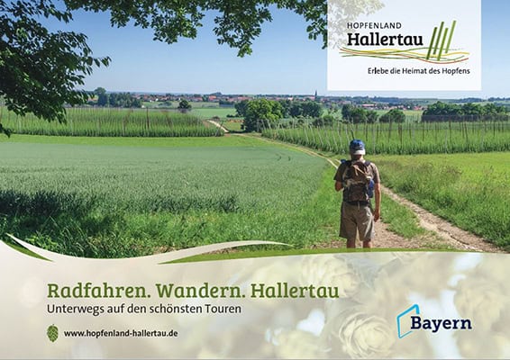 Cover - Radfahren Wandern Hallertau Eine Person läuft auf einem Feldweg durch saftig grüne Felder unter blauem Himmel. Ein Text auf dem Bild wirbt für Radfahren und Wandern in der Hallertau und betont deren Verbindung zum Hopfen. Es gibt Logos für Hopfenland Hallertau und Bayern.