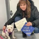 Puppy graduate with handler holding diploma, celebrating success at High Plains K-9 Connections dog training program.