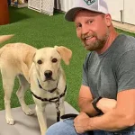 A man smiling with a service dog at High Plains K-9 Connections, demonstrating professional dog training and therapy dog services in a friendly, supportive environment.