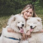 Fluffy white Great Pyrenees dogs with a smiling woman outdoors in a natural setting, highlighting dog training and therapy services at High Plains K-9 Connections.