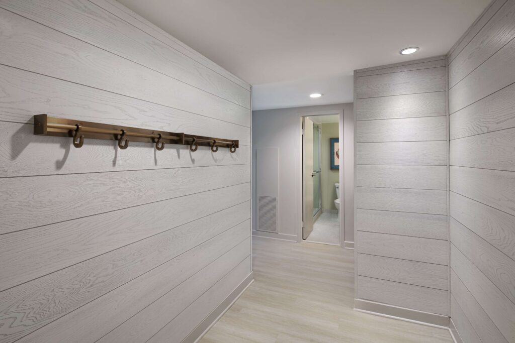 Hallway with wooden paneling and coat hooks leading to a bathroom.