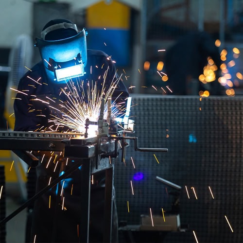 Welding process on fabricated material with sparks flying in an industrial setting.