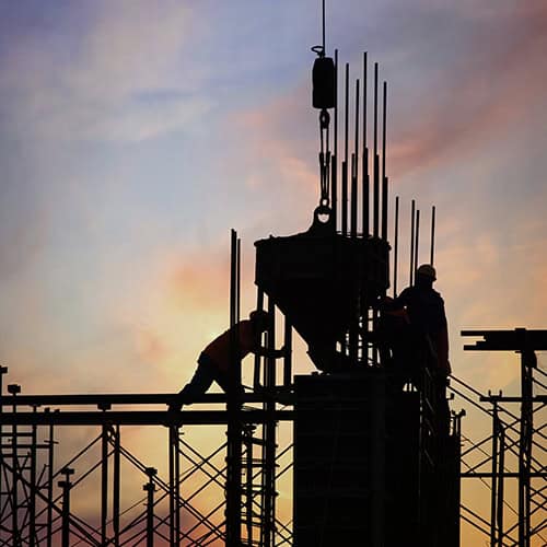 Construction workers installing steel reinforcement at a high-rise building site during sunset.