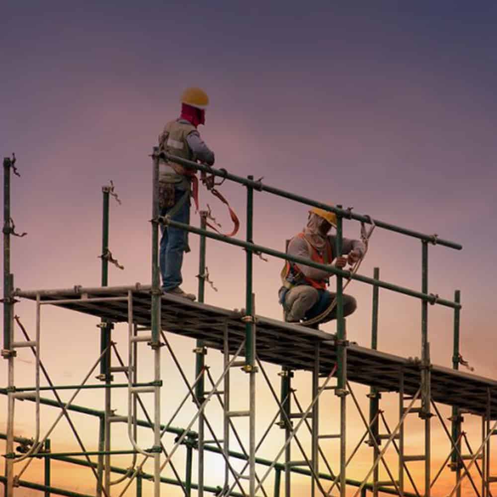Construction workers working on scaffolding during sunset at a building site.