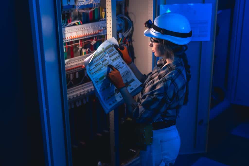 electrician inspecting electrical switchboard using technical blueprint industrial energy system (1)