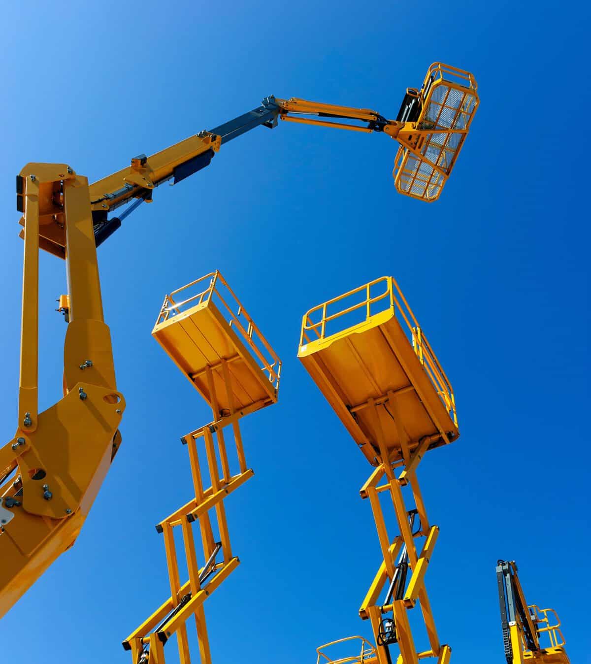 Das Bild zeigt zahlreiche gelbe Arbeitsbühnen, die auf einem großen Freigelände stehen und ihre Plattformen weit in den blauen Himmel ausfahren. Sie symbolisieren unsere vielfältige Mietflotte für anspruchsvolle Arbeiten in der Höhe. Viele gelbe Arbeitsbühnen, die hoch in den Himmel ragen.