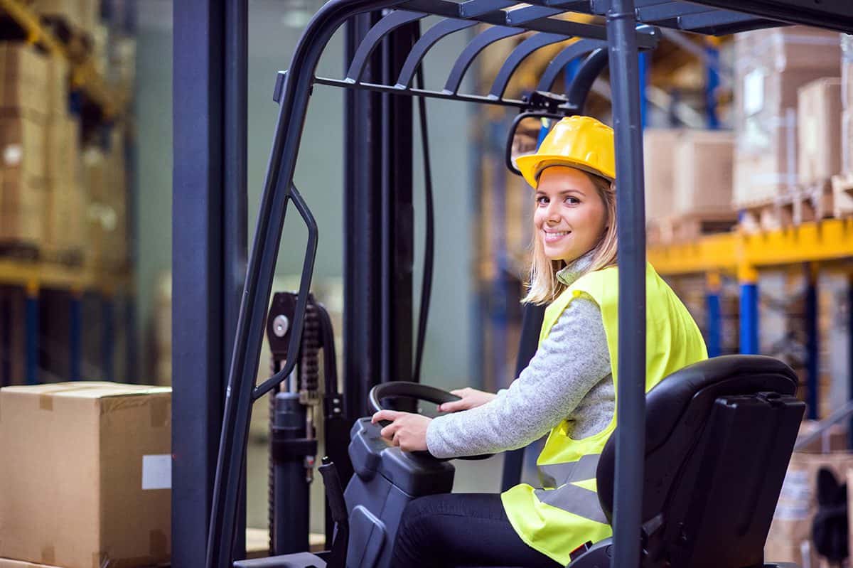Das Bild zeigt eine Frau, die aufmerksam in einem Gabelstapler sitzt und die Steuerung bedient. Sie demonstriert Kompetenz und Sicherheit bei der Arbeit mit dem Gerät, symbolisiert die professionelle Handhabung unserer Mietmaschinen. Frau sitzt konzentriert in einem Gabelstapler und bedient ihn
