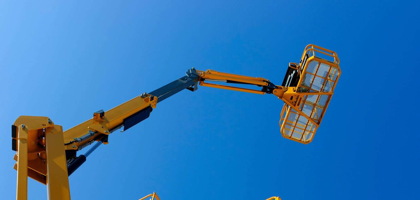 Das Bild zeigt zahlreiche gelbe Scherenbühnen, die nebeneinander aufgestellt sind und weit in den klaren blauen Himmel hinausragen. Die Scherenbühnen sind moderne Arbeitsbühnen, die für Arbeiten in großer Höhe verwendet werden, etwa bei Bau- oder Wartungsarbeiten. Durch ihre leuchtend gelbe Farbe heben sie sich deutlich vom Hintergrund ab. Mehrere gelbe Scherenbühnen, die hoch in den blauen Himmel ragen.