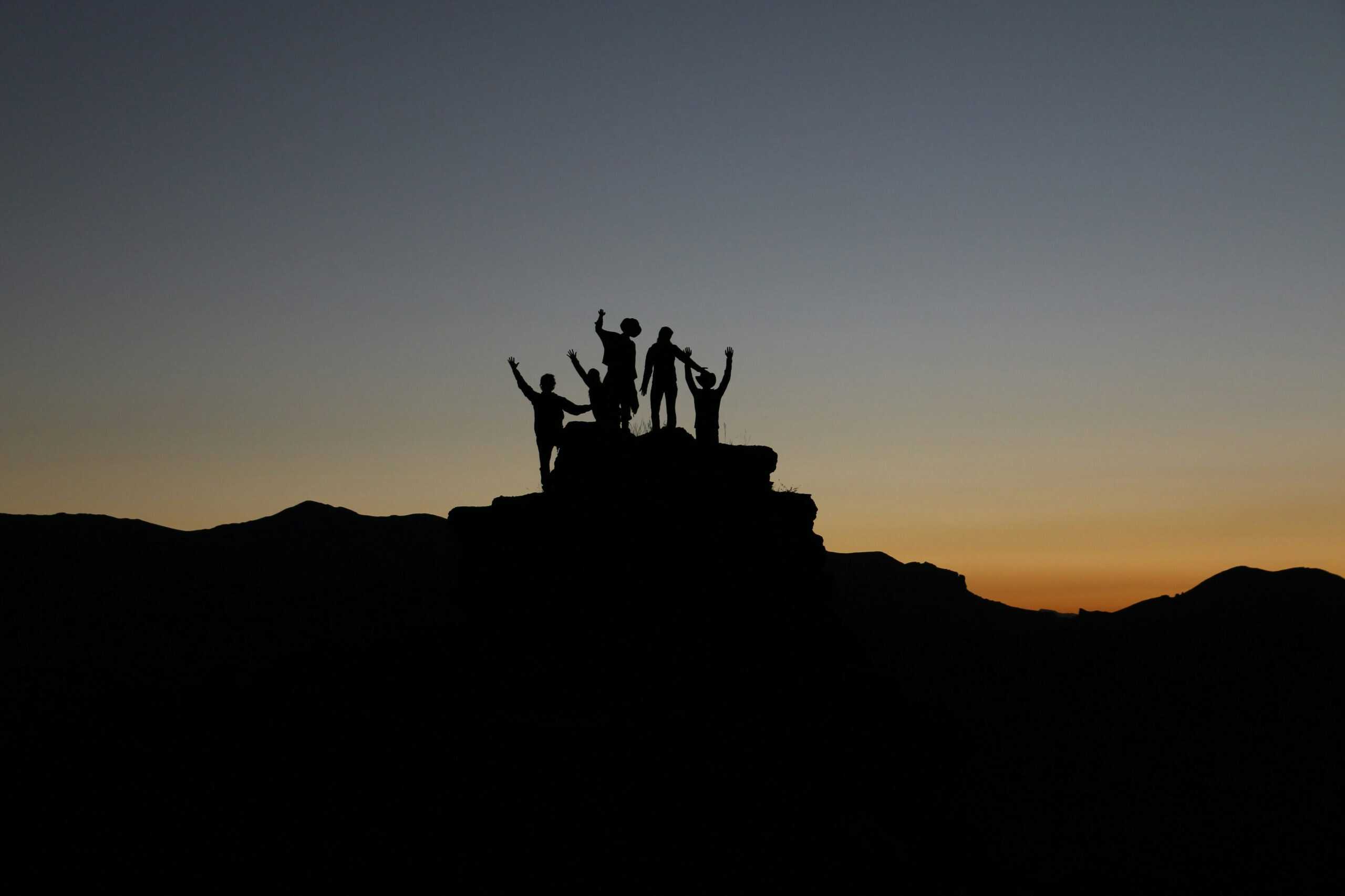 Menschen auf Berggipfel im Abendlicht – Symbol für Gemeinschaft und Zusammenhalt.