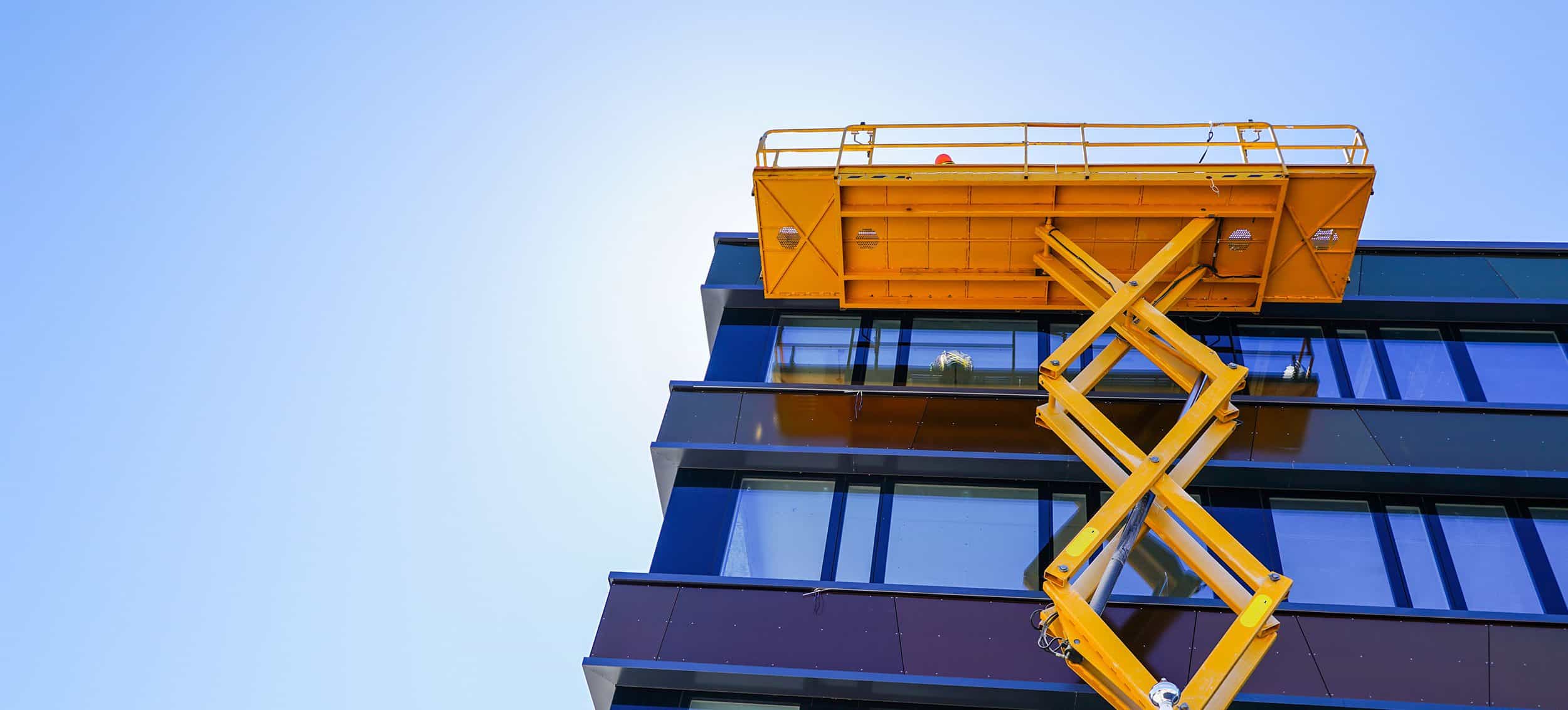 Gelbe Scherenarbeitsbühne vor modernem Hochhaus mit blauer Glasfassade.