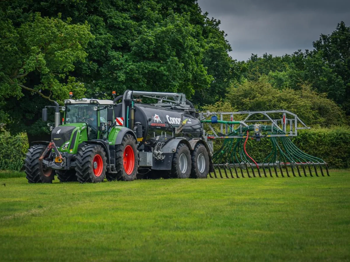 Fendt with black connor tanker on Green tractor with fertilizer spreader on grass field.