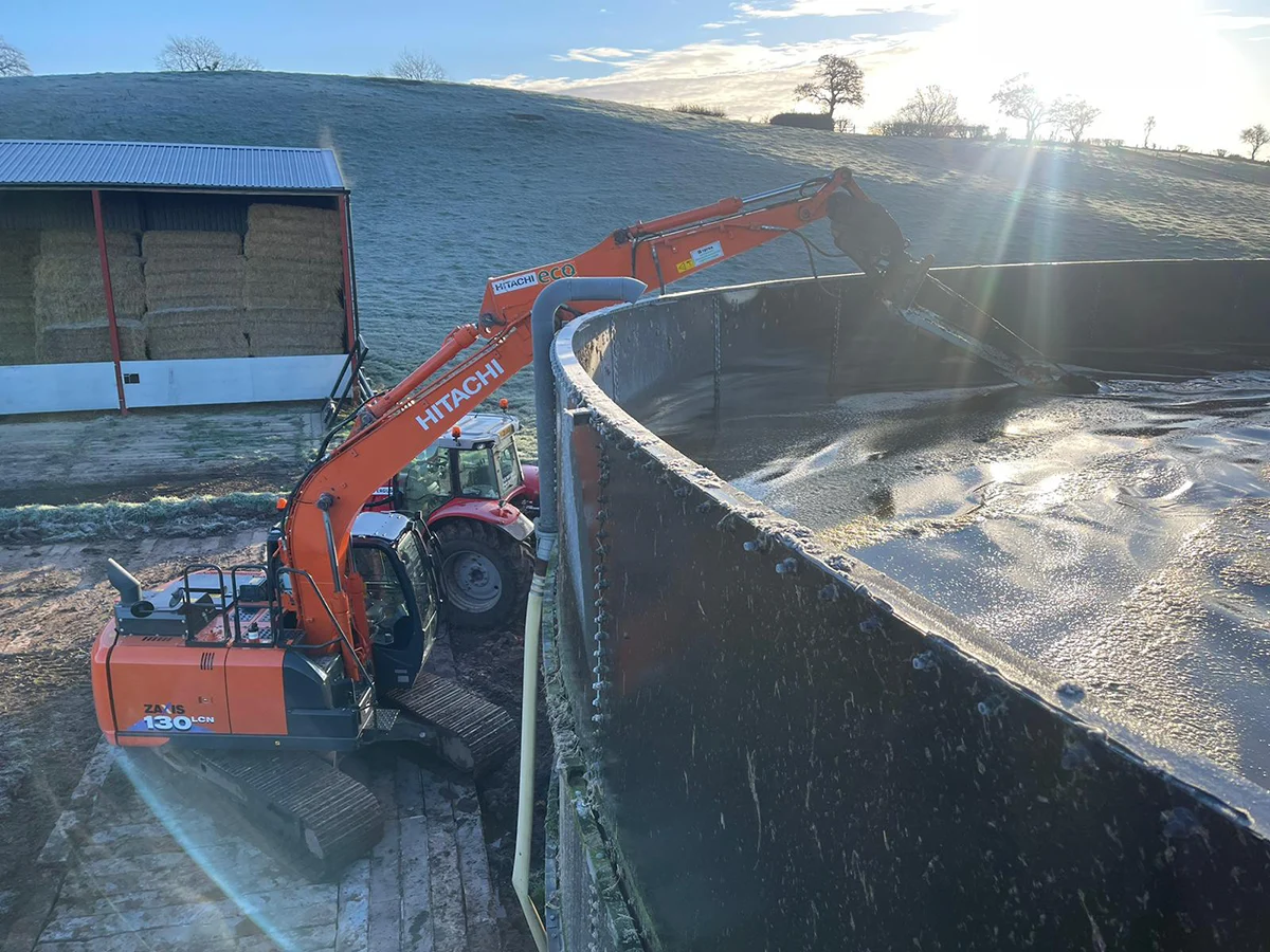digger with tower stirer Excavator filling large black tank with liquid.