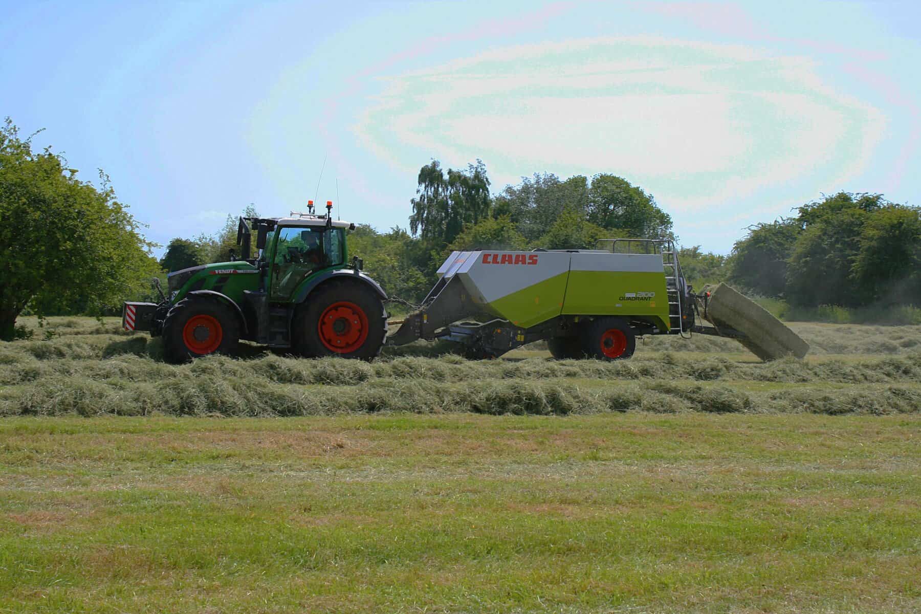 Tractor baling hay in sunny field.