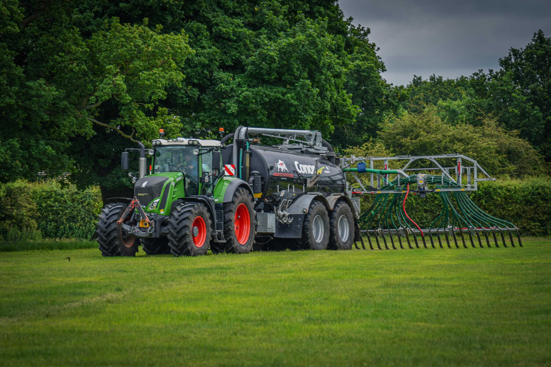 Green tractor spreading fertilizer on grass field.