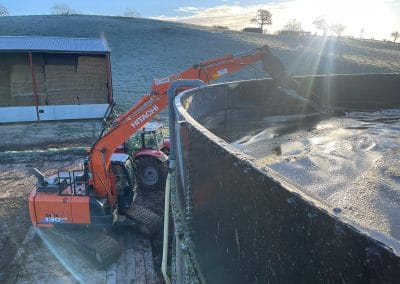 Excavator stirring large water tank on a farm.