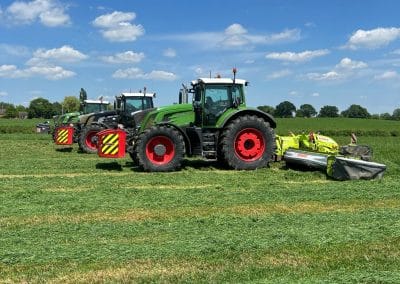 Tractors mowing green field under blue sky.