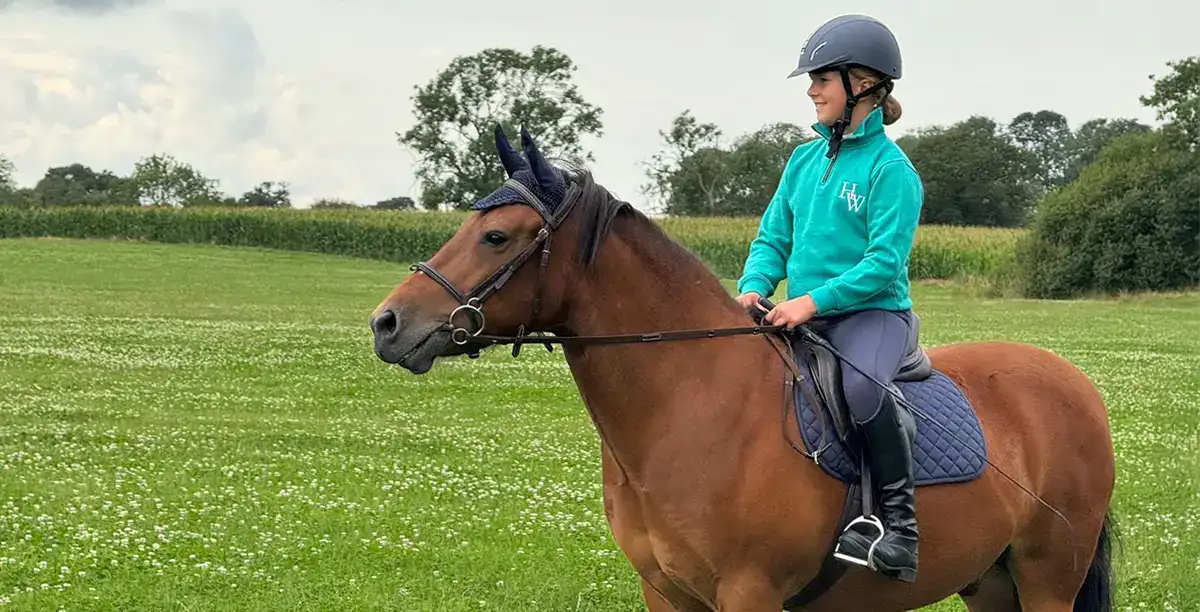 Child riding horse in green field.