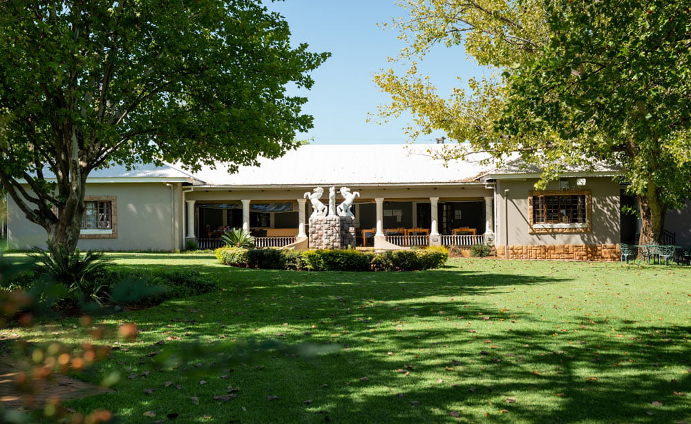 Serene exterior of Hope Again Wellness Center featuring lush green lawn, mature trees, and a welcoming building with a cozy porch, ideal for mental health and wellness support.
