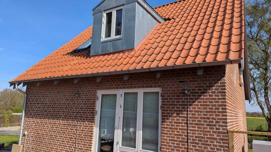 Rødt tegltag med en grå zinkkvist og et vindue.