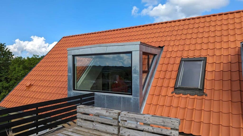 Grå zinkkvist monteret på et rødt tegltag med udsigt til himlen.