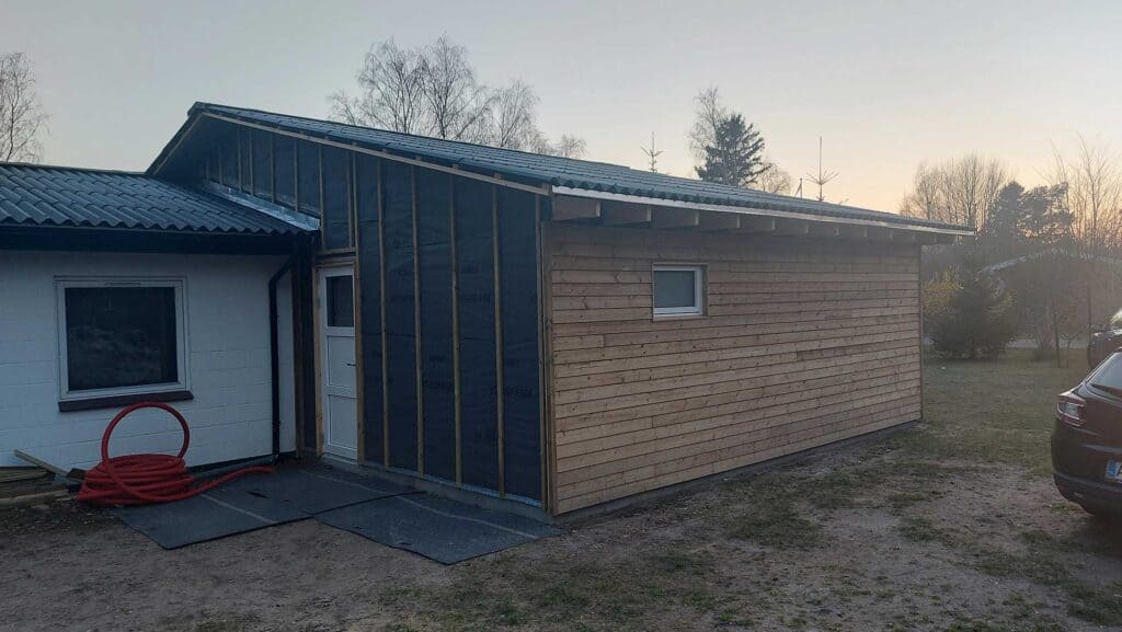 Mindre tilbygning med lodret, sort træbeklædning og et lille vindue.