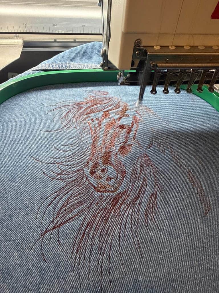 Embroidery machine stitching a detailed lion portrait on denim fabric.