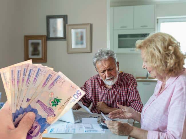 Imagen de una pareja de adultos mayores revisando documentos y dinero en efectivo en un ambiente hogareño, ilustrando los cambios en las pensiones en Colombia desde 2025.