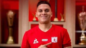 Juan Fernando Quintero, jugador de la Selección Colombia, con camiseta roja, en un entorno de estudio con trofeos en el fondo.
