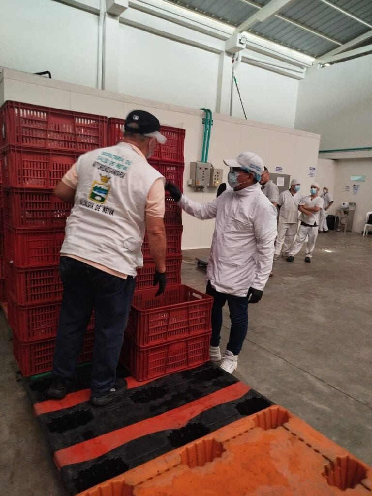 Trabajadores inspeccionando cajas de productos en un ambiente industrial en Huila Tv, garantizando calidad y seguridad en la manipulación de alimentos en Neiva, Colombia.
