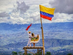 1. Bandera de Colombia en paisaje montañoso con pareja cultural en la cima del bambú, celebrando tradiciones y patrimonio en Huila.