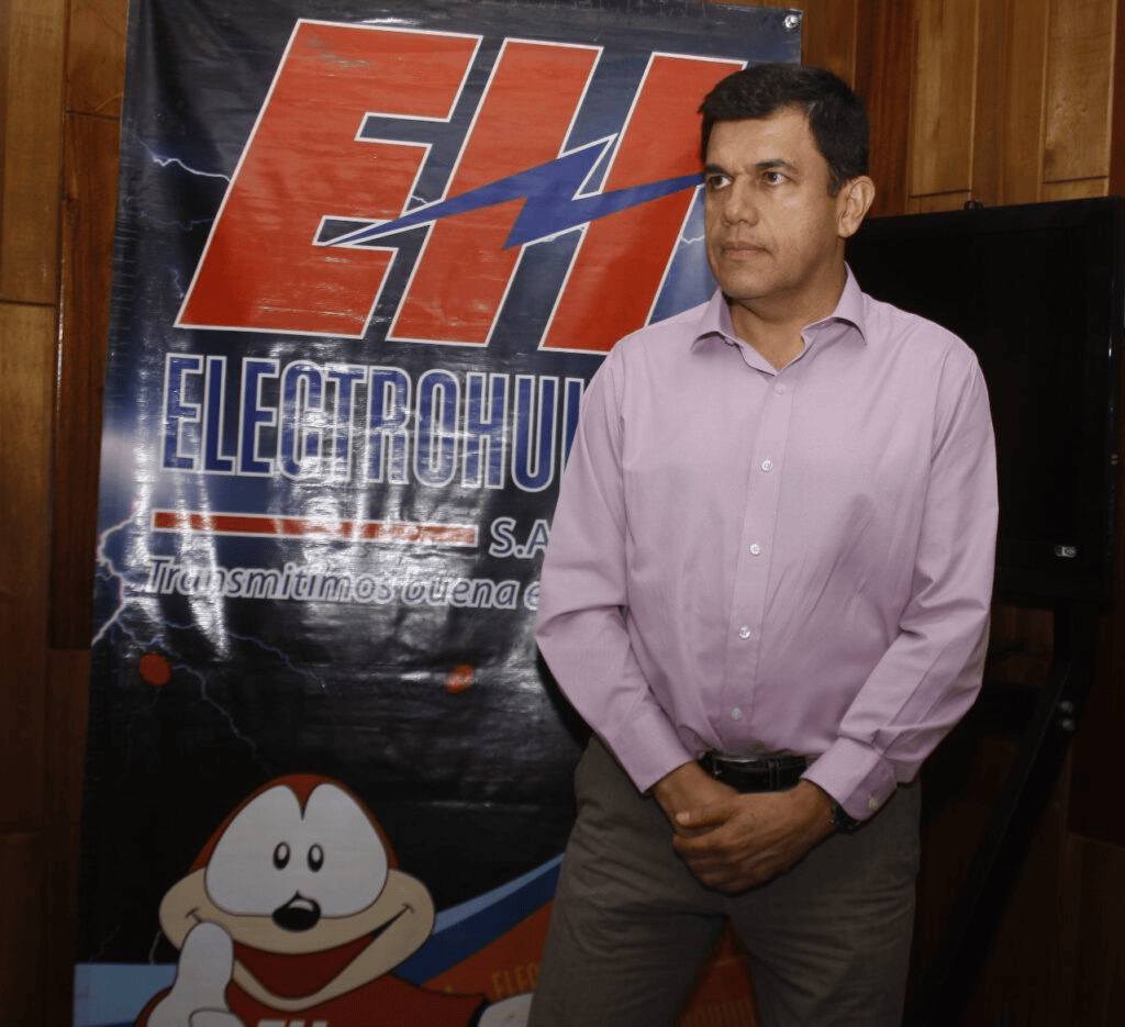 1. Hombre en evento de Huila TV, transmisión de energía eléctrica en Colombia, frente a cartel oficial, en ambiente profesional y formal.