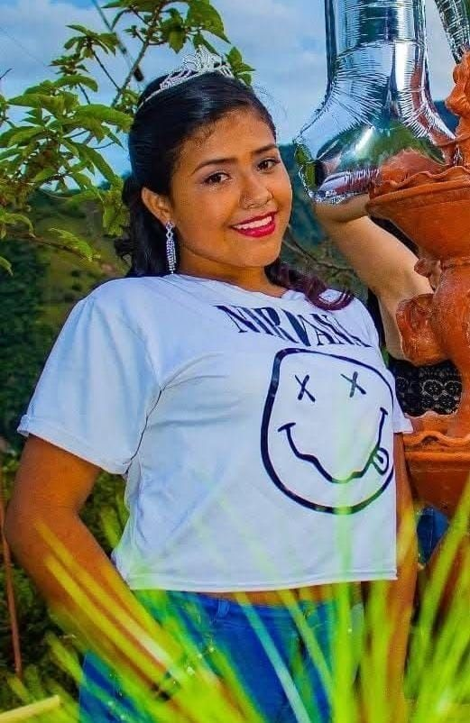 Niña sonriendo con camiseta de estilo casual, rodeada de naturaleza y plantas, en un ambiente al aire libre, con elementos decorativos en cerámica, en un contexto que refleja cultura y alegría en Huila, Colombia.