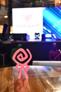 1.Figura decorativa de color rosa en forma de símbolo artístico en una mesa de madera, en un evento o exposición con pantalla LED y ambiente moderno y tecnológico.