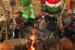 1. Personas indígenas de Huila participando en ceremonia cultural tradicional con fuego y vestimenta típica en un evento en un espacio de madera artesanal.