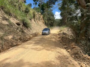 Autopista rural en Huila, Colombia, con auto compacto transitando por camino sin pavimentar rodeado de vegetación tropical y montañas.